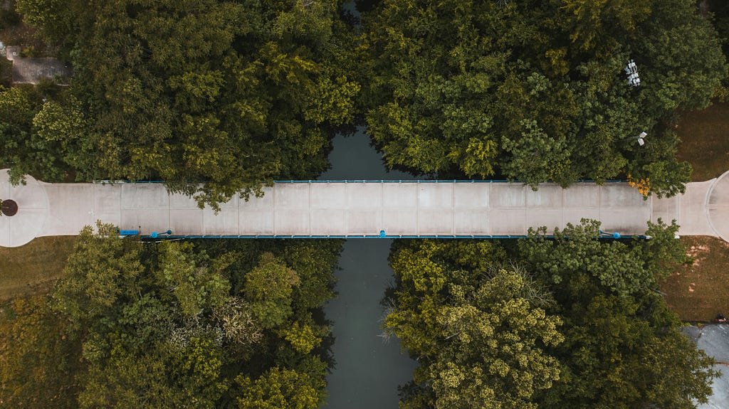 Birds eye view of a bridge over a river between 2 tree areas